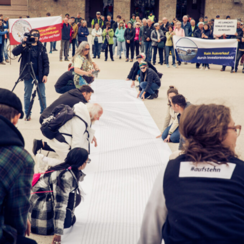 Auf dem Bild sind etwa 10 Menschen zu sehen, die eine Meterlange Schriftrolle festhalten. Darauf abgebildet sind die Namen der 170.000 Unterstützer_innen der Petition gegen die Gletscher-Ehe Pitzal-Ötztal.