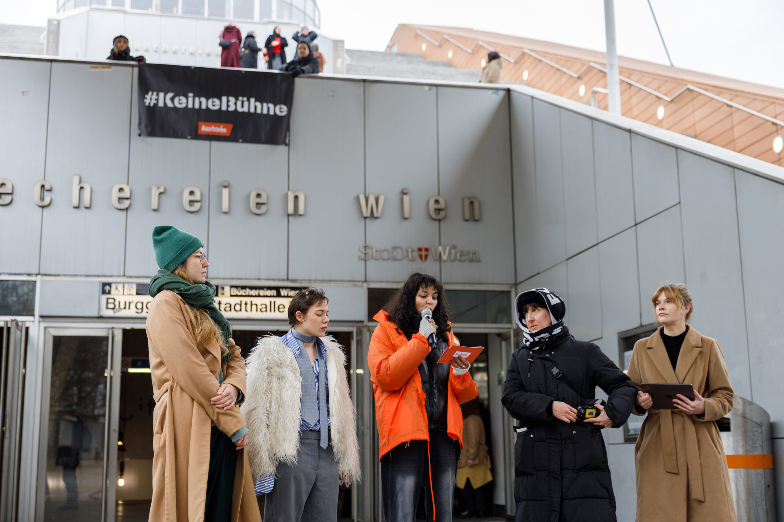 Auf dem Bild sind die Expert_innen Dr.in Yara Hofbauer, Sophie Tschannett, die Catcalls of Vienna und Moderatorin Fatima Jost von #aufstehn während der Aktion zu sehen. Im Hintergrund ist das #KeineBühne Banner sichtbar, wie es über dem Eingang zur U-Bahn-Station Burggasse/Stadthalle gehängt wird.